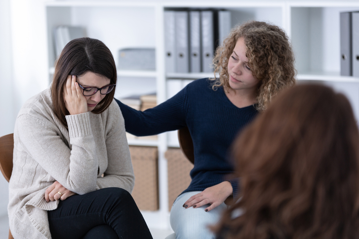 Young woman supporting sad patient at Women's issues support group